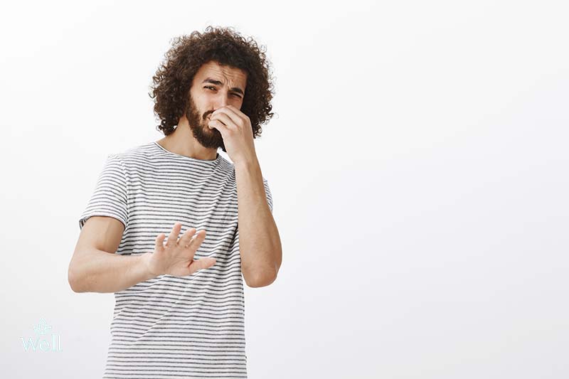You stink, do not come closer. Portrait of disgusted disliking handsome guy with afro hairstyle, tilting backwards and pulling palm in stop or no gesture, covering nose from awful smell over gray wall.