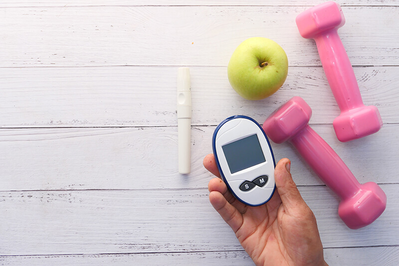 Apple and dumbbells on a table, representing healthy lifestyle tools for diabetics.